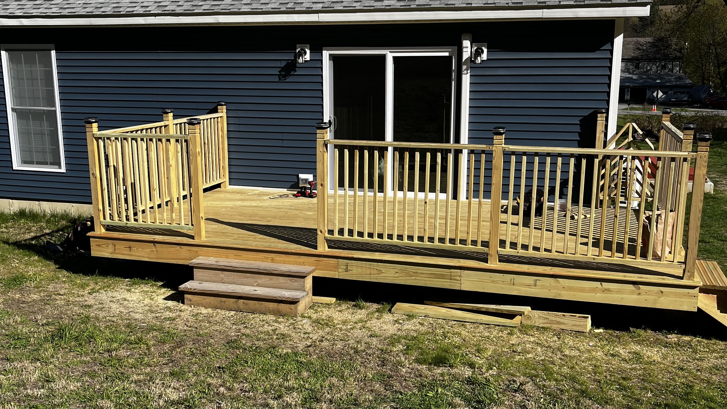 Wood deck with railings and front steps alongside a blue-sided home.